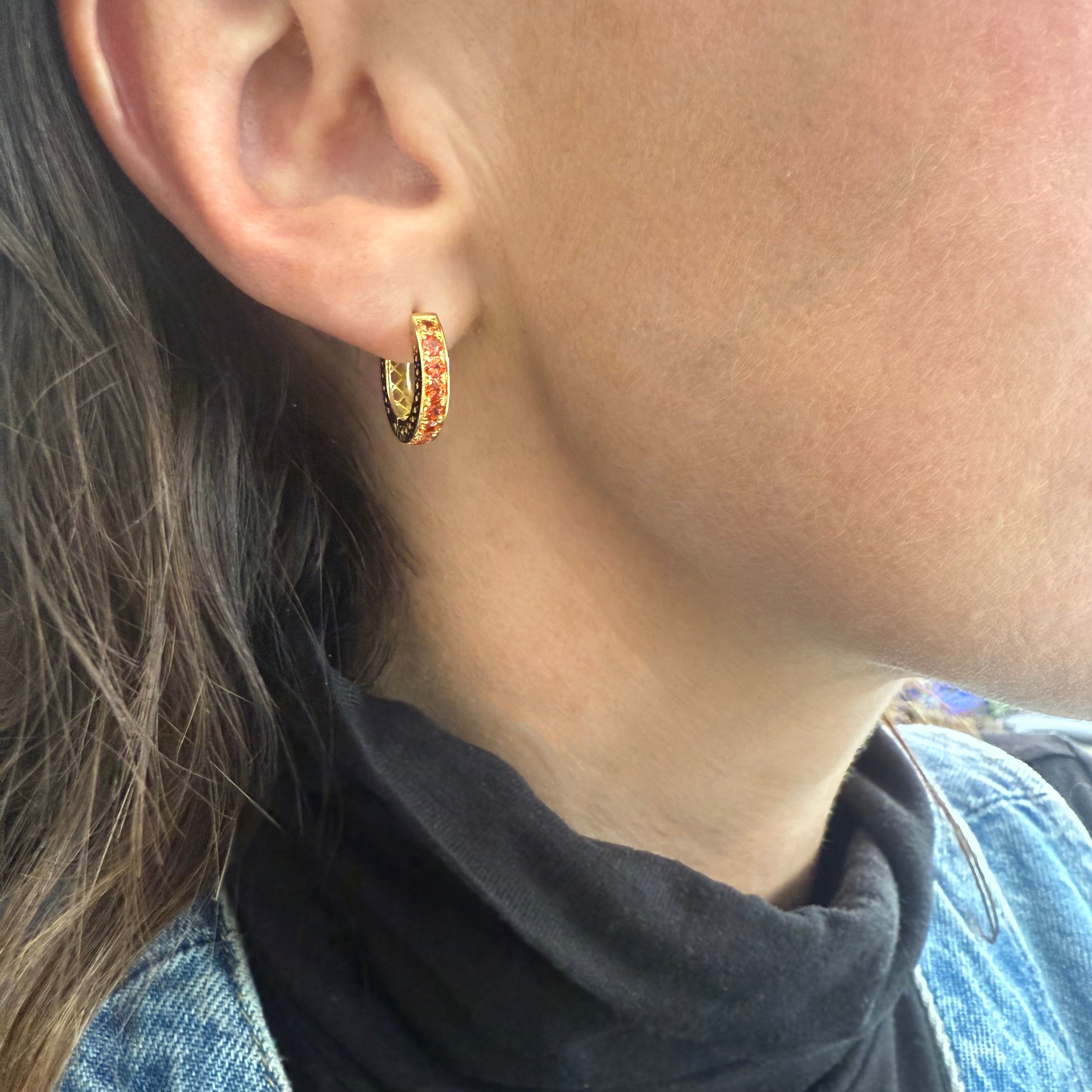 Close-up of an ear wearing a gold hoop earring with orange stones.