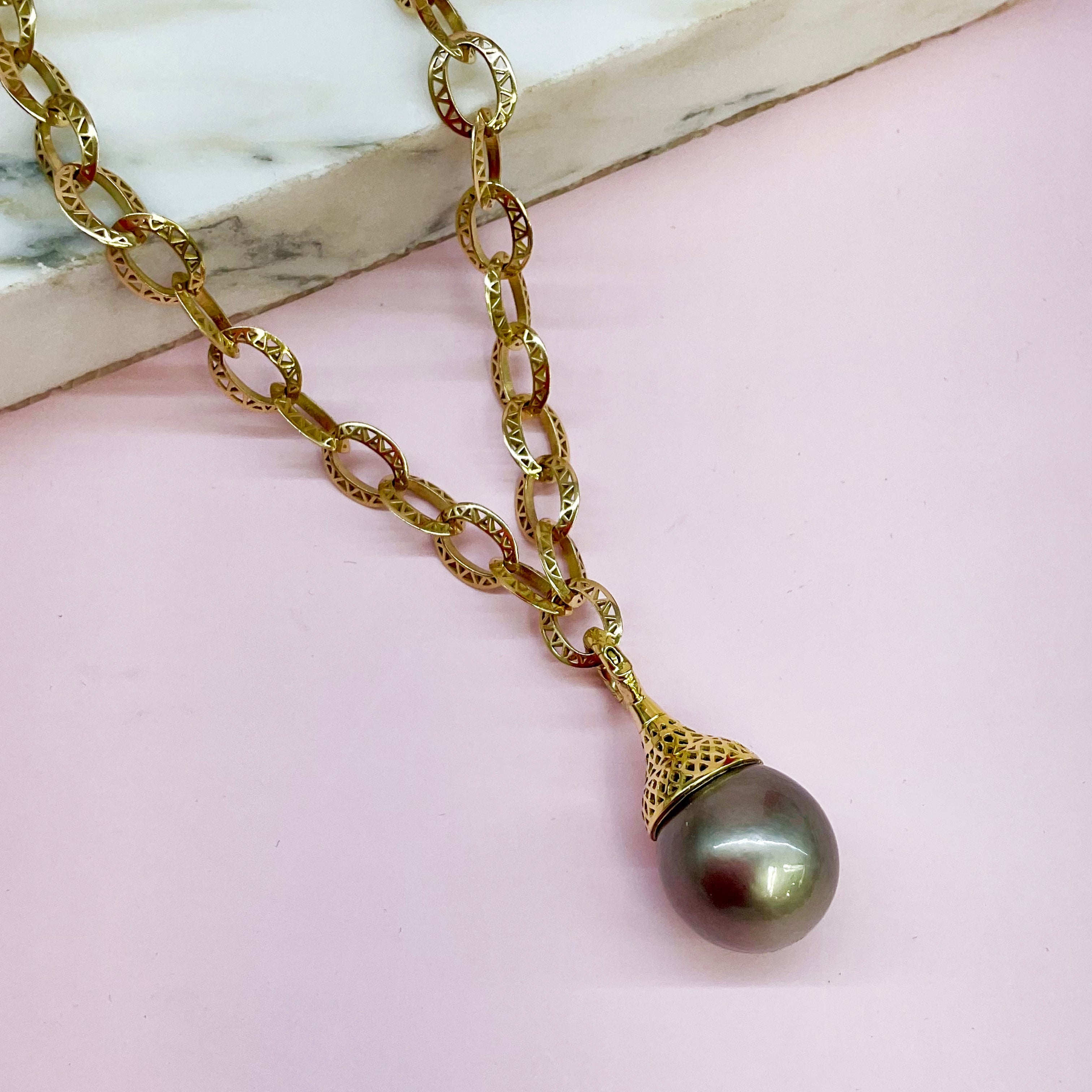Gold necklace with a Tahitian pearl pendant on a pink surface