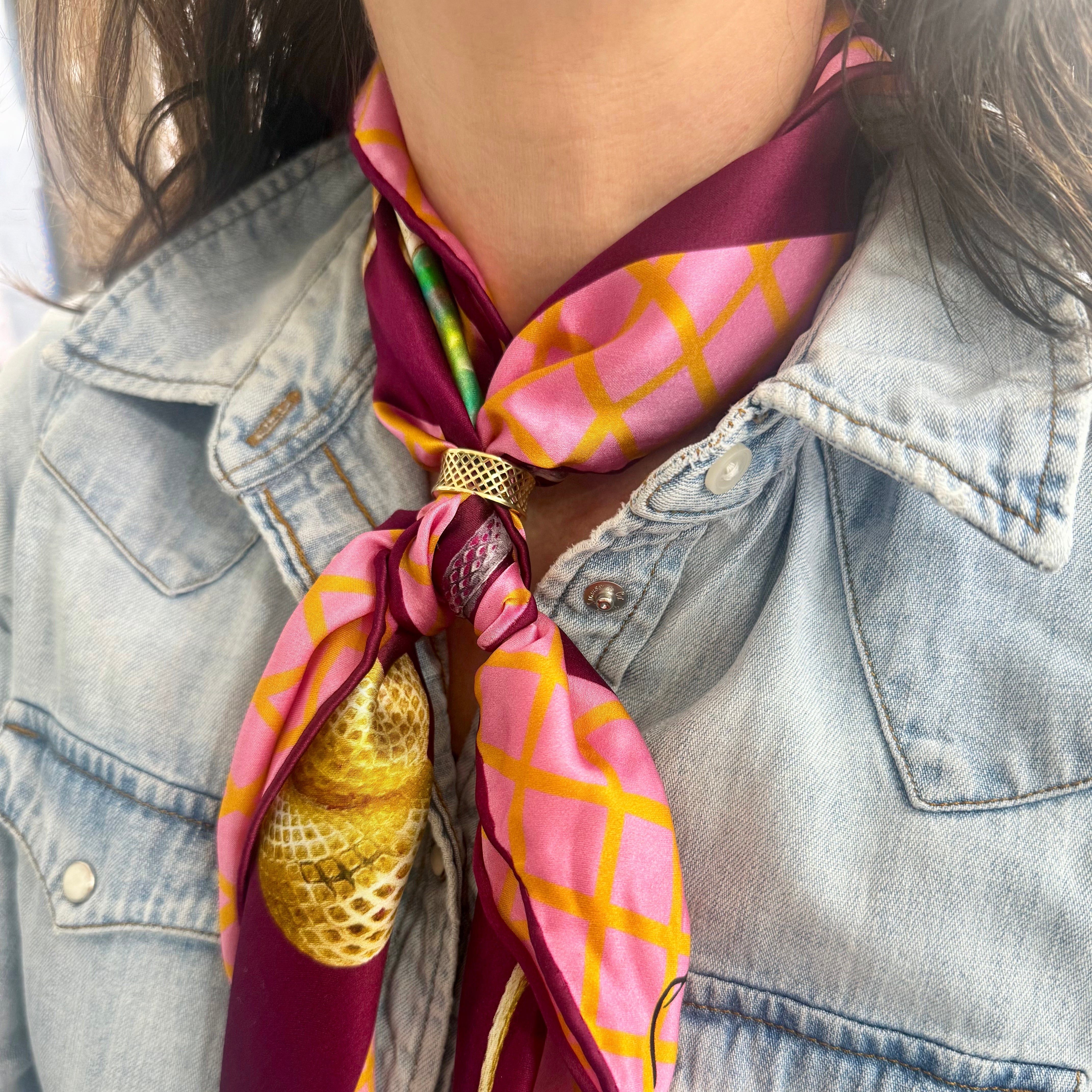 Person wearing a colorful scarf with geometric pattern and gold accessory on denim jacket.