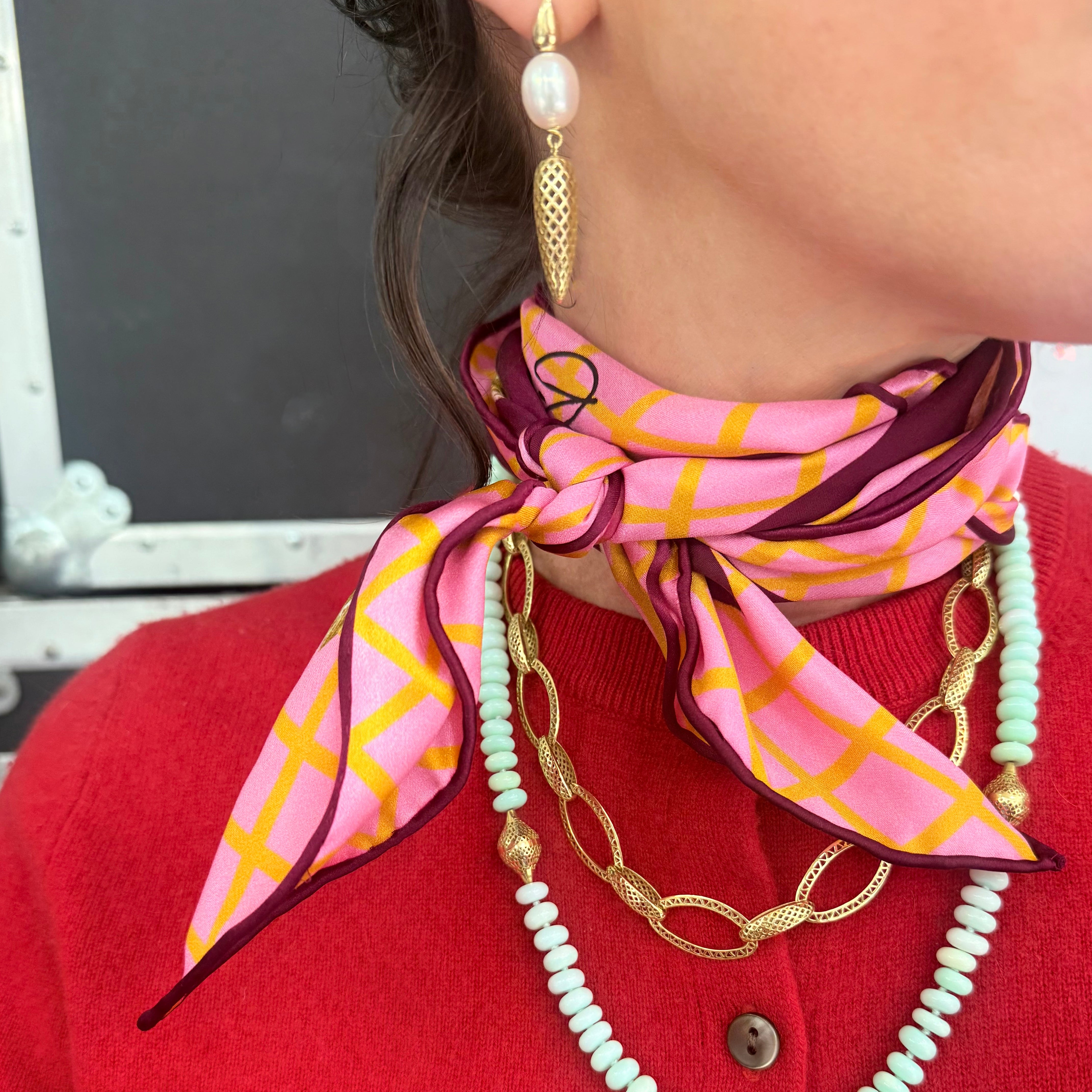 Person wearing a pink and orange patterned scarf, gold necklace, and pearl earrings.