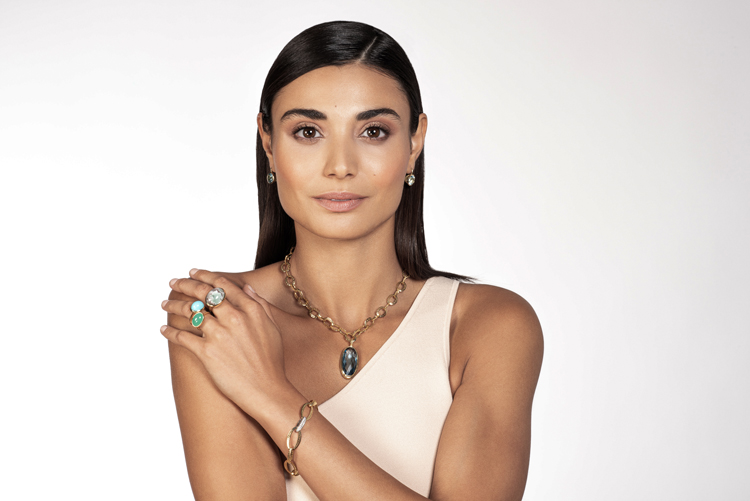 This is an image of a model wearing a necklace and pendant with stacks of rings on her fingers