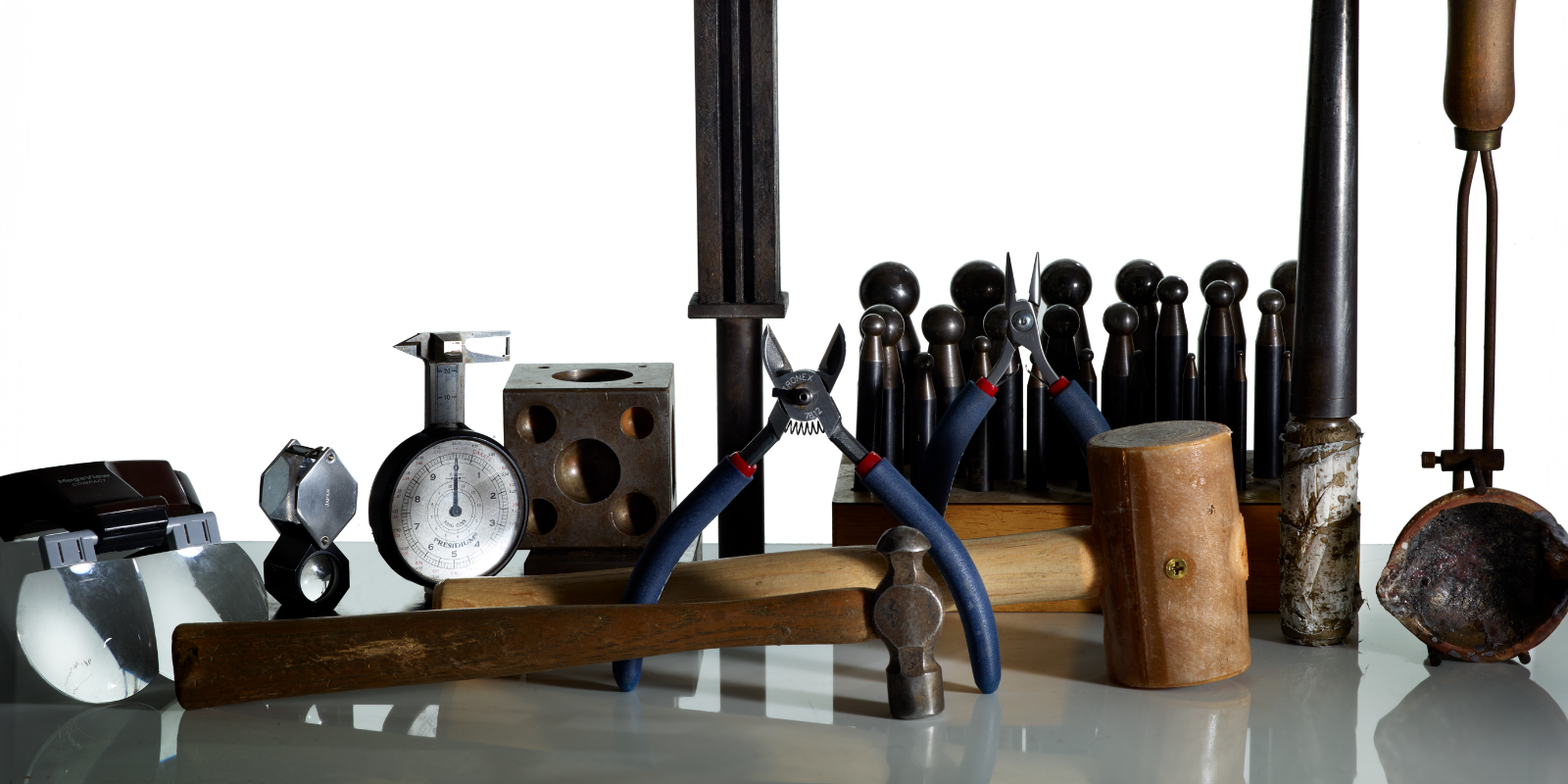 Collection of tools including pliers, hammers, and weights on a reflective surface.