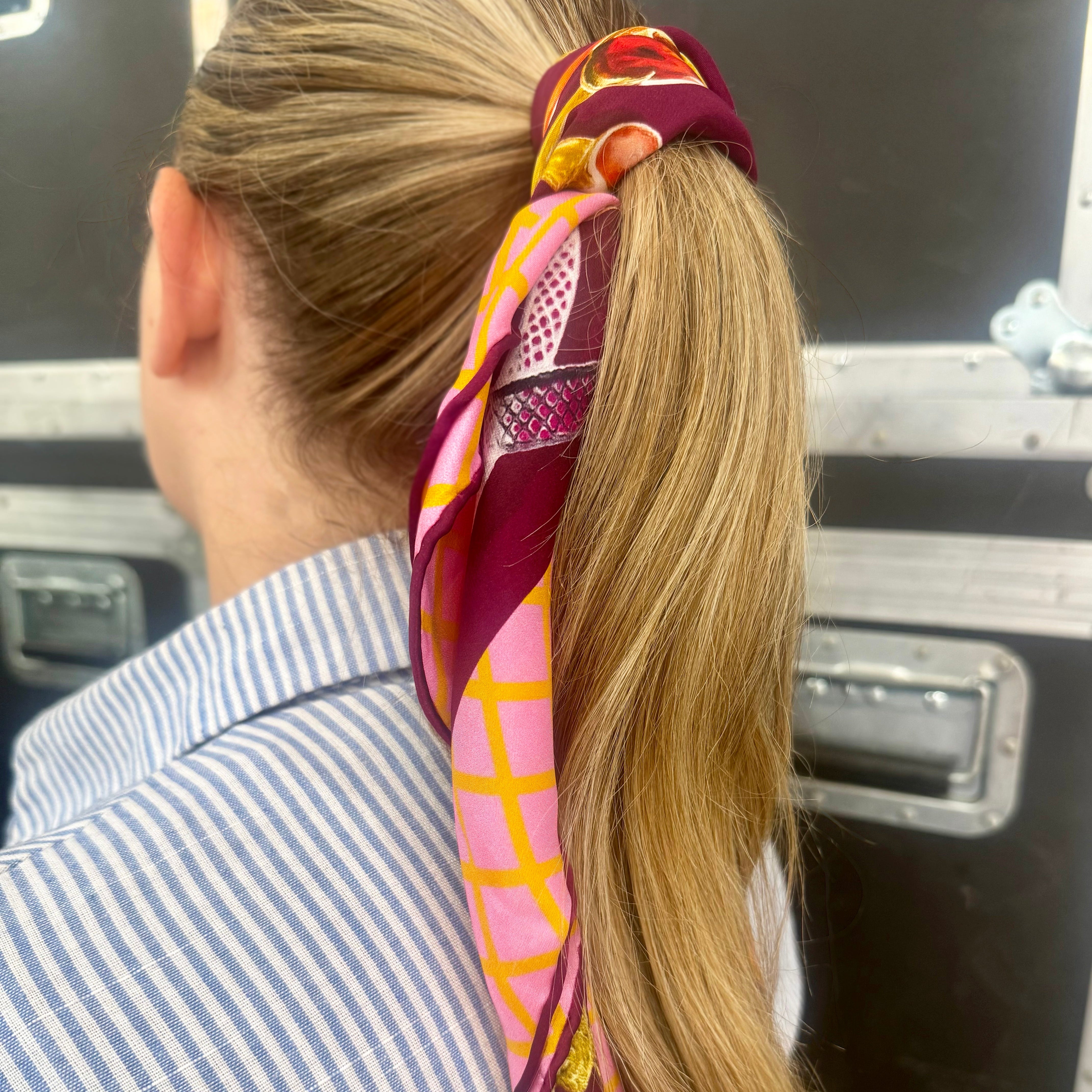 Person with a colorful scarf tied around their ponytail, standing in front of a metallic surface.