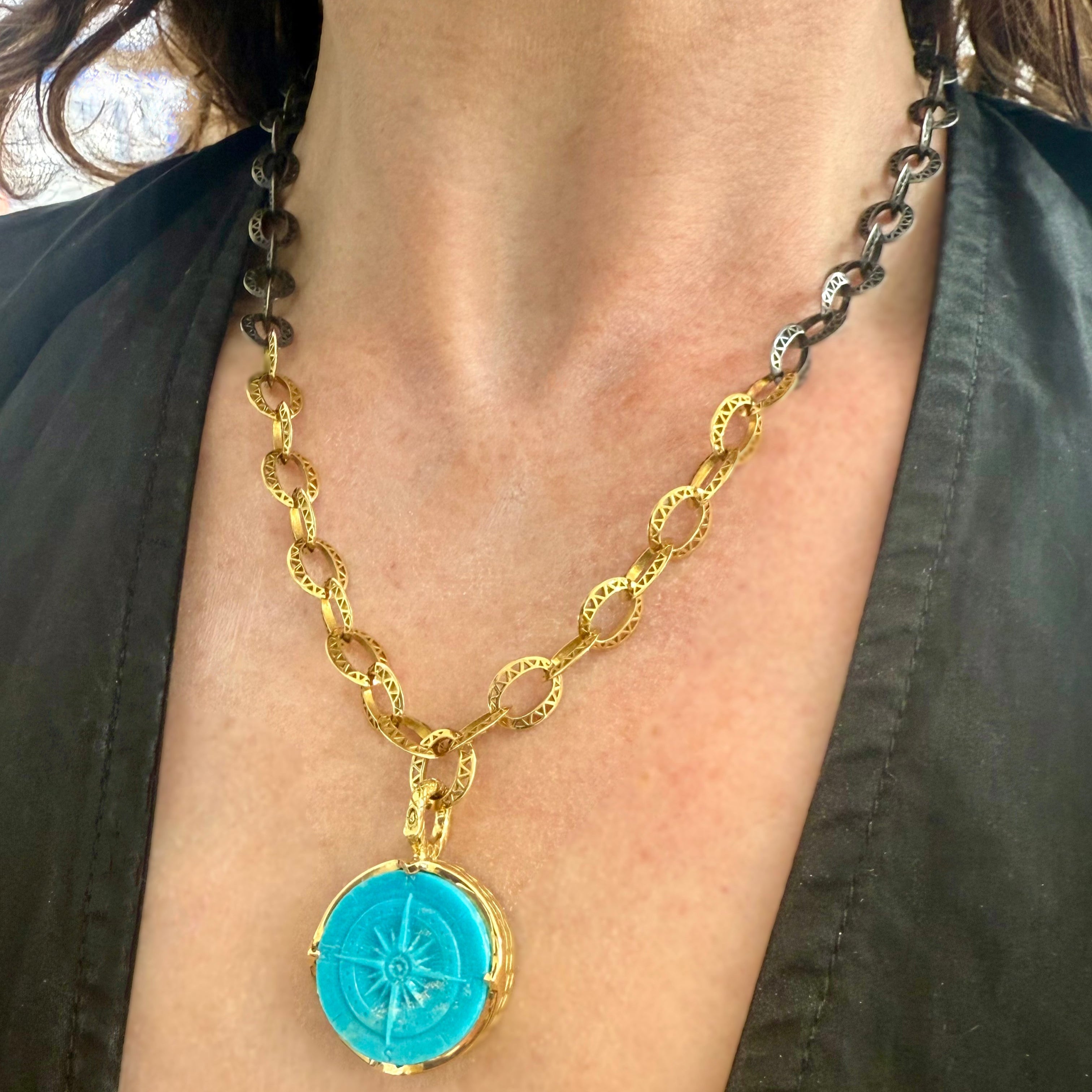 Gold chain necklace with a blue pendant on a person wearing a dark green top.