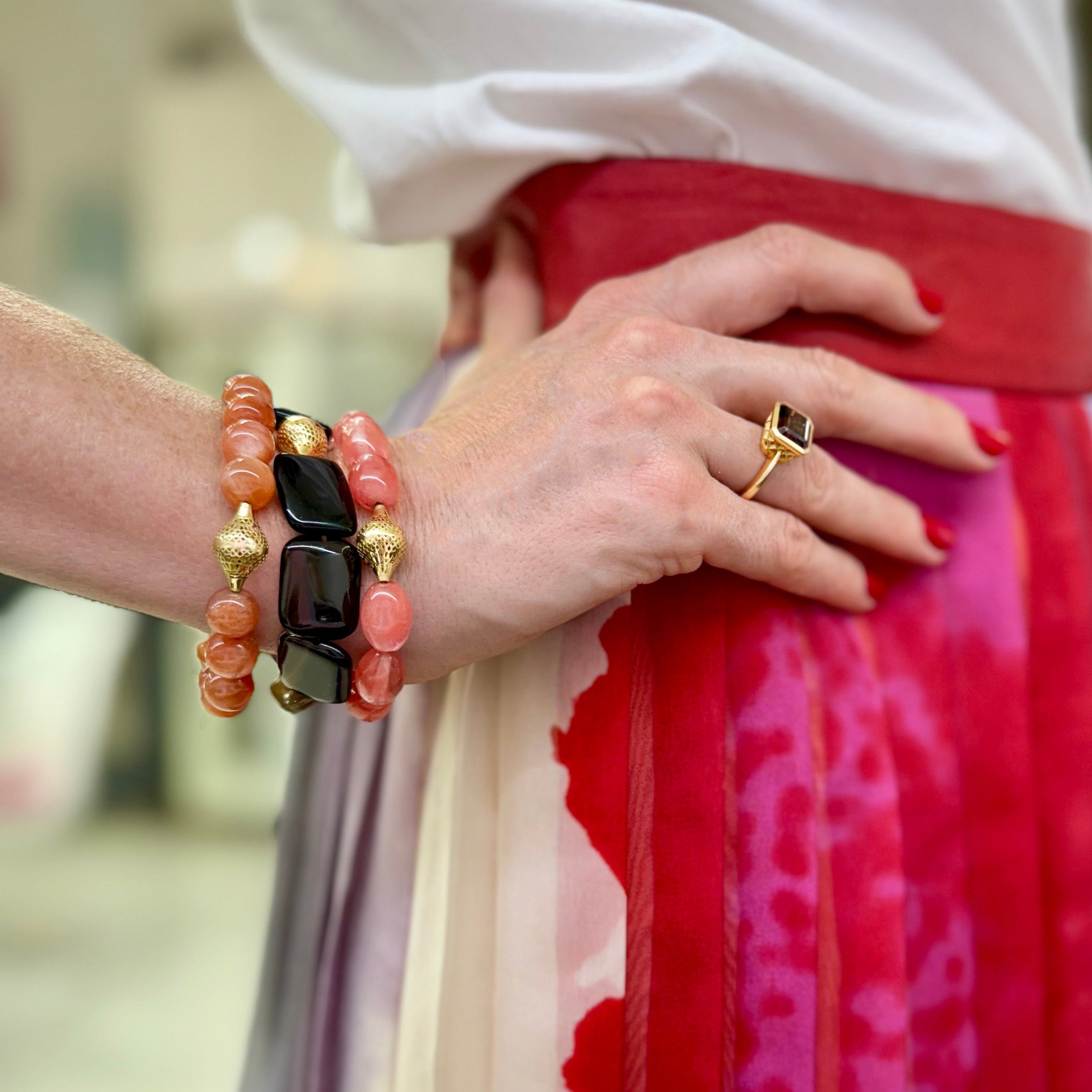 Close-up of a person wearing brown zircon ring and a stack of bracelets a with a blurred background