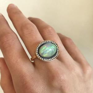 This is an image of an opal ring with diamonds surround set in oxidized silver =- The shank of the ring is 18k Yellow Gold 