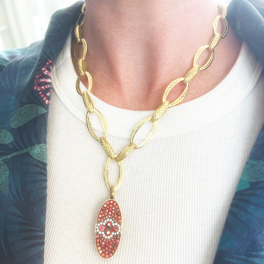 This is an image of an orange sapphire and diamond pendant being worn on a gold necklace