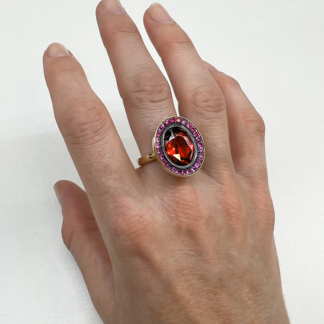 This image shows our north/south cocktail ring with a garnet center and pink sapphire surrounding stones being worn on a middle finger