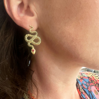 This is an image of 18k Yellow Gold earrings with red sapphires being worn on the ear