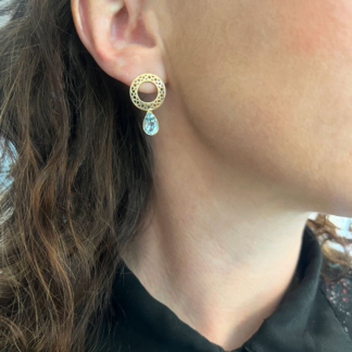 These are gold hoop earrings on a post being worn with bezel set blue topaz pear shaped drops