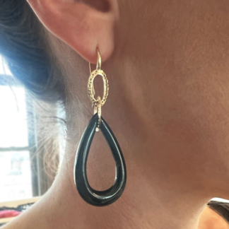 This is an image if a pair of black onyx earrings carved into a pair shape with oval gold links being worn to show how they hang