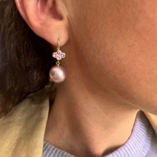 This is an image of the model wearing a pearl drop earring with 4 pink sapphires set in a clover on the yellow gold hook