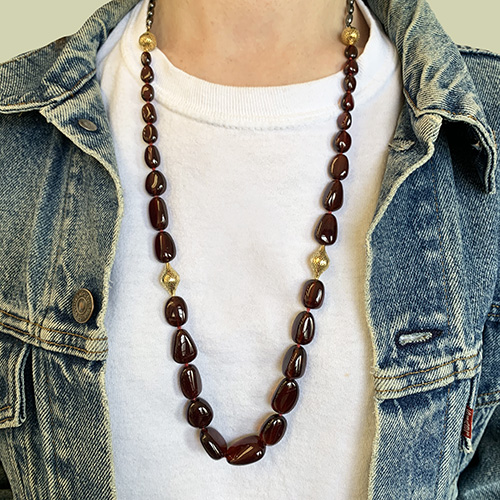 This is a photo of a tumbled garnet beaded necklace with small gold finials with white T-shirt and denim jacket