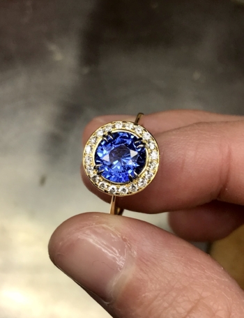 This is a photo of an 18k yellow gold 10mm Crownwork claw set Blue Sapphire ring with pave diamond surround