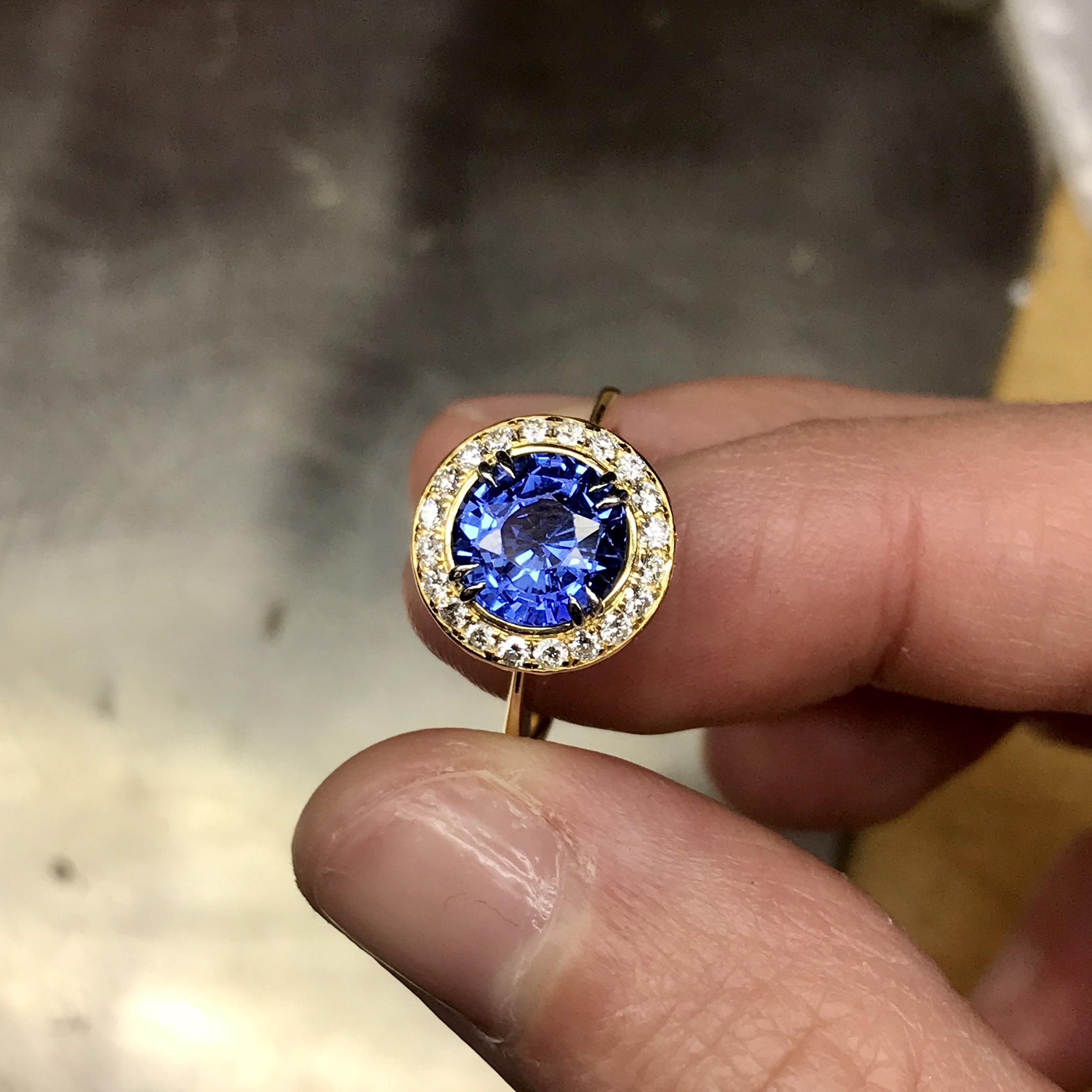 This is a photo of an 18k yellow gold 10mm Crownwork claw set Blue Sapphire ring with pave diamond surround