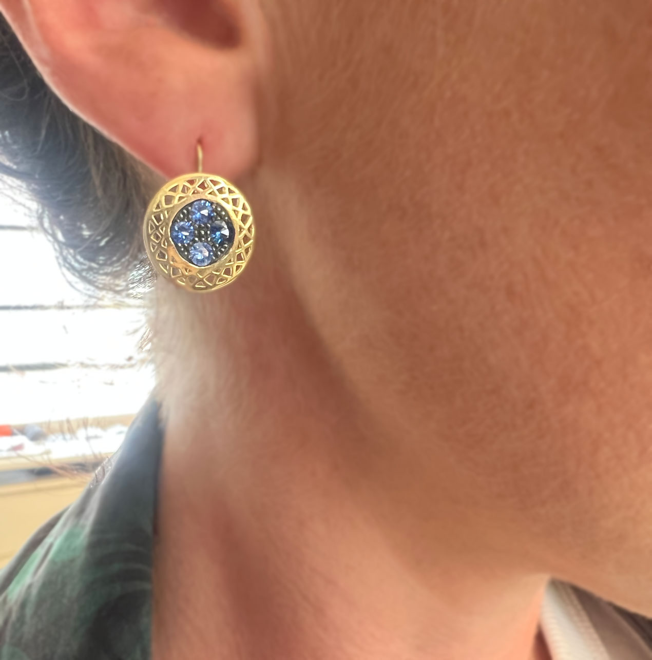 18k yellow gold Round crownwork disc set with blue sapphires in oxidized silver on hooks being worn on the ear