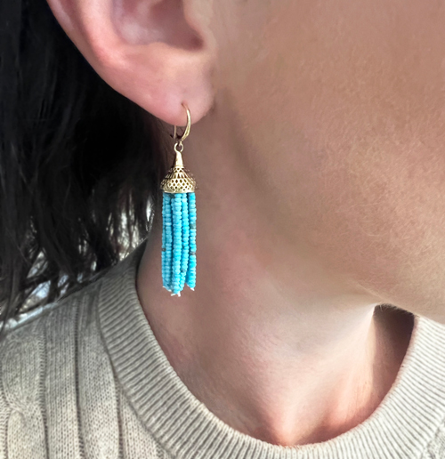 This is a photo of a pair of turquoise tassel drop earrings with a gold top on wires being worn by a model