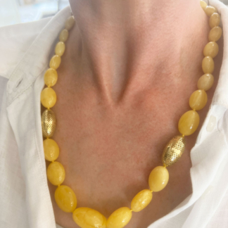 This is photo of a graduated amber necklace with two 18k yellow gold olive beads worn with a white shirt.